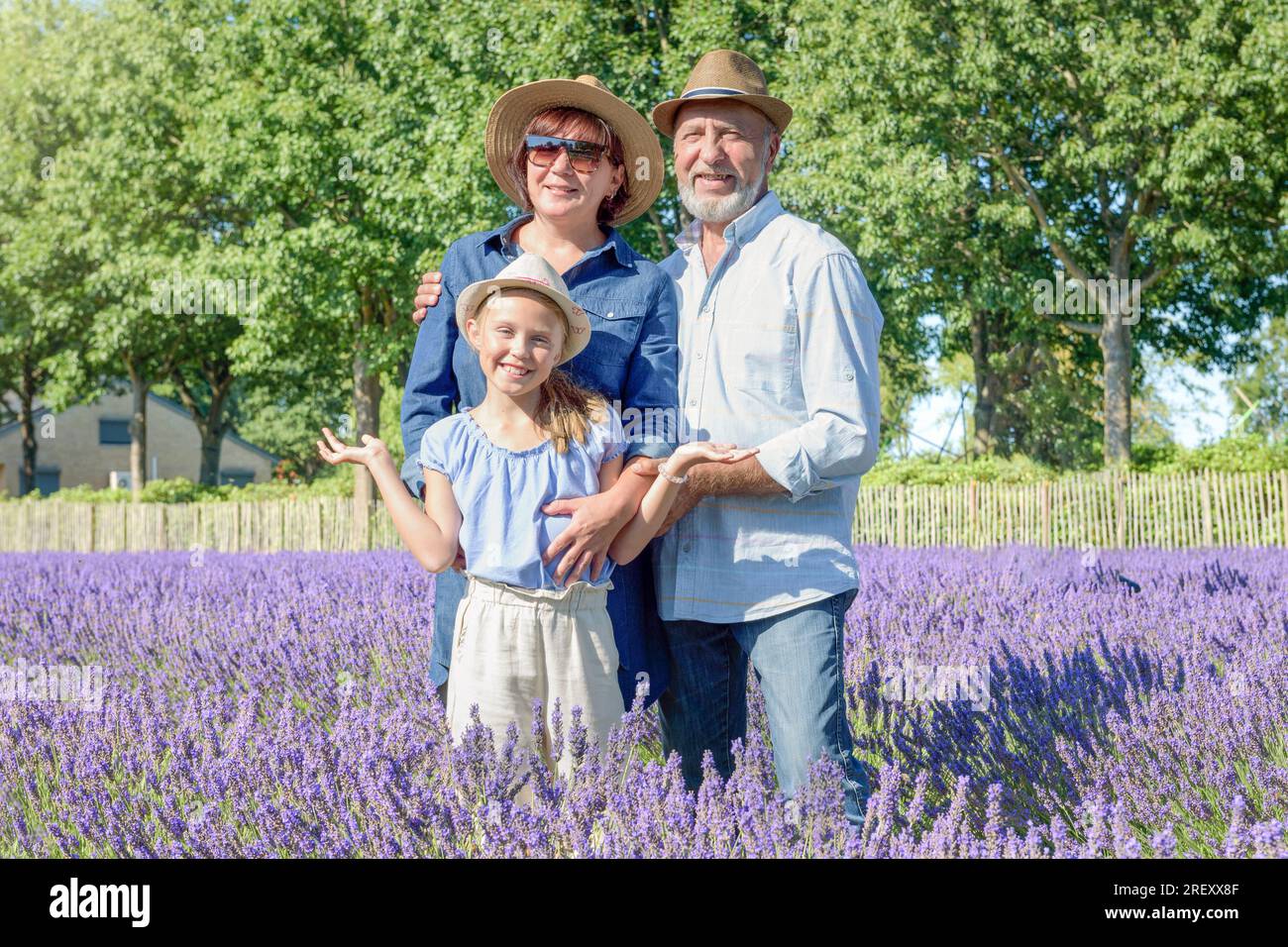 Happy family in a lavender field in bloom. Man woman and girl standing on fresh aromatic plantation beds in sunny day. Blue sky natural background Stock Photo
