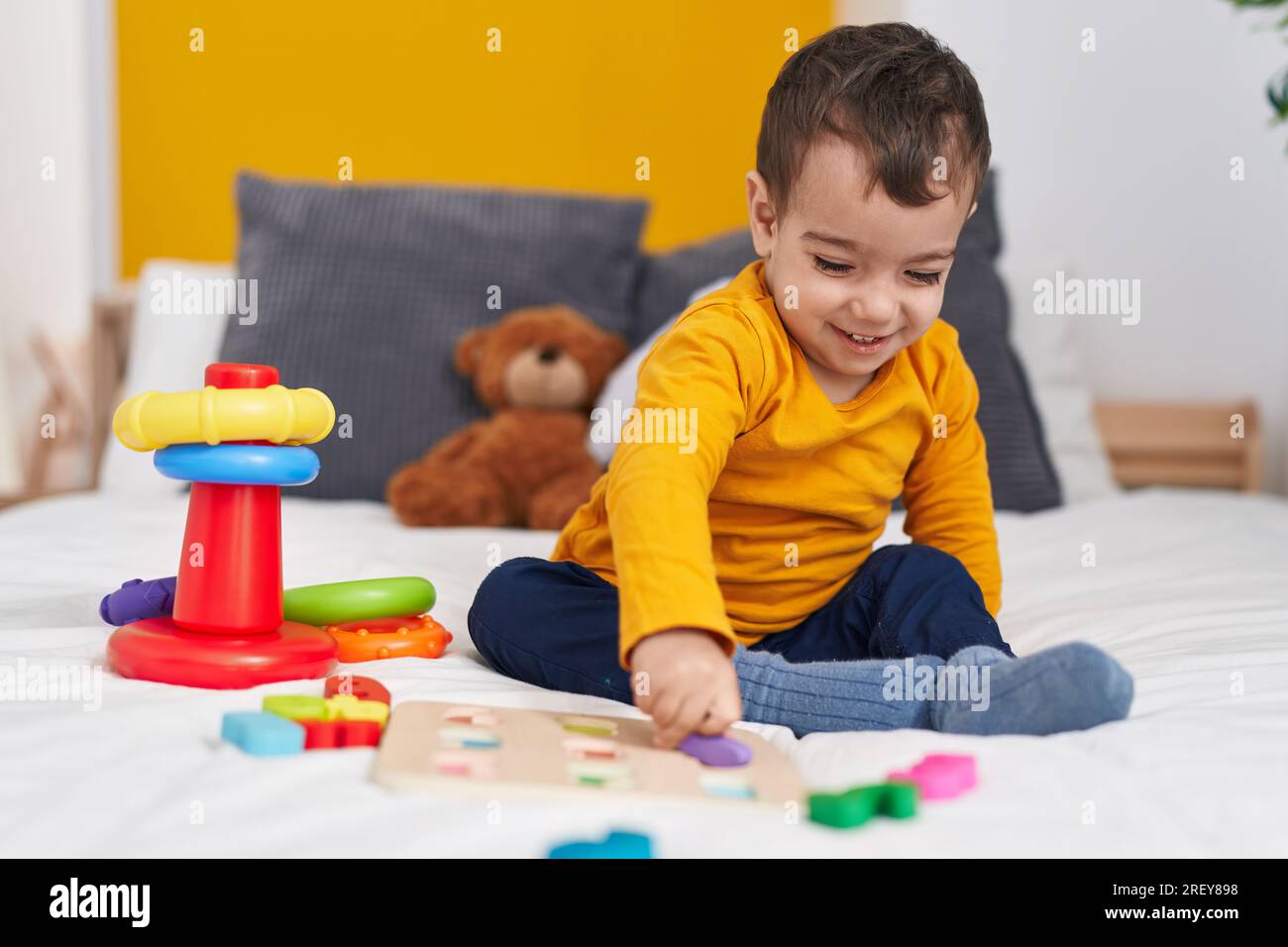 Adorable hispanic boy playing with maths puzzle game sitting on bed at ...