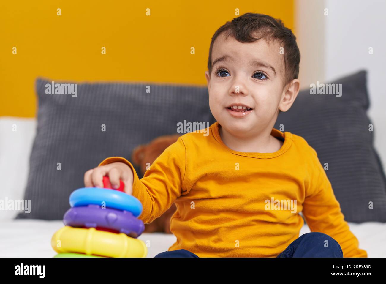 Adorable hispanic boy playing with hoops game sitting on bed at bedroom ...