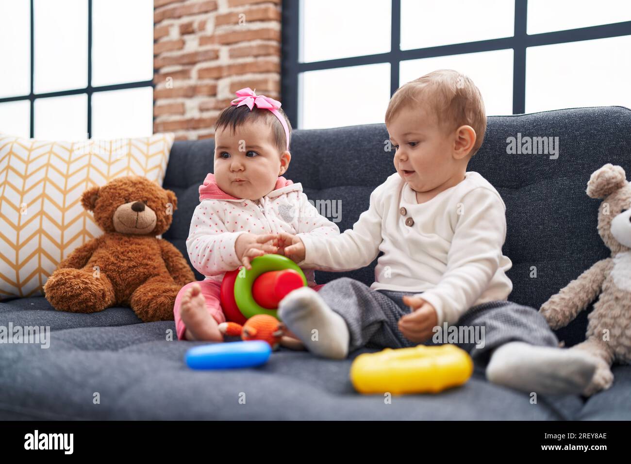 Adorable boy and girl playing with hoops game sitting on sofa at home ...