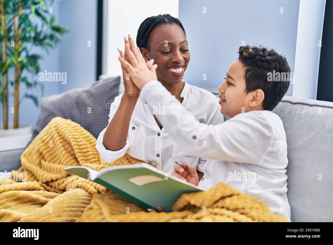 African american mother and son doing homework sitting on sofa at home ...