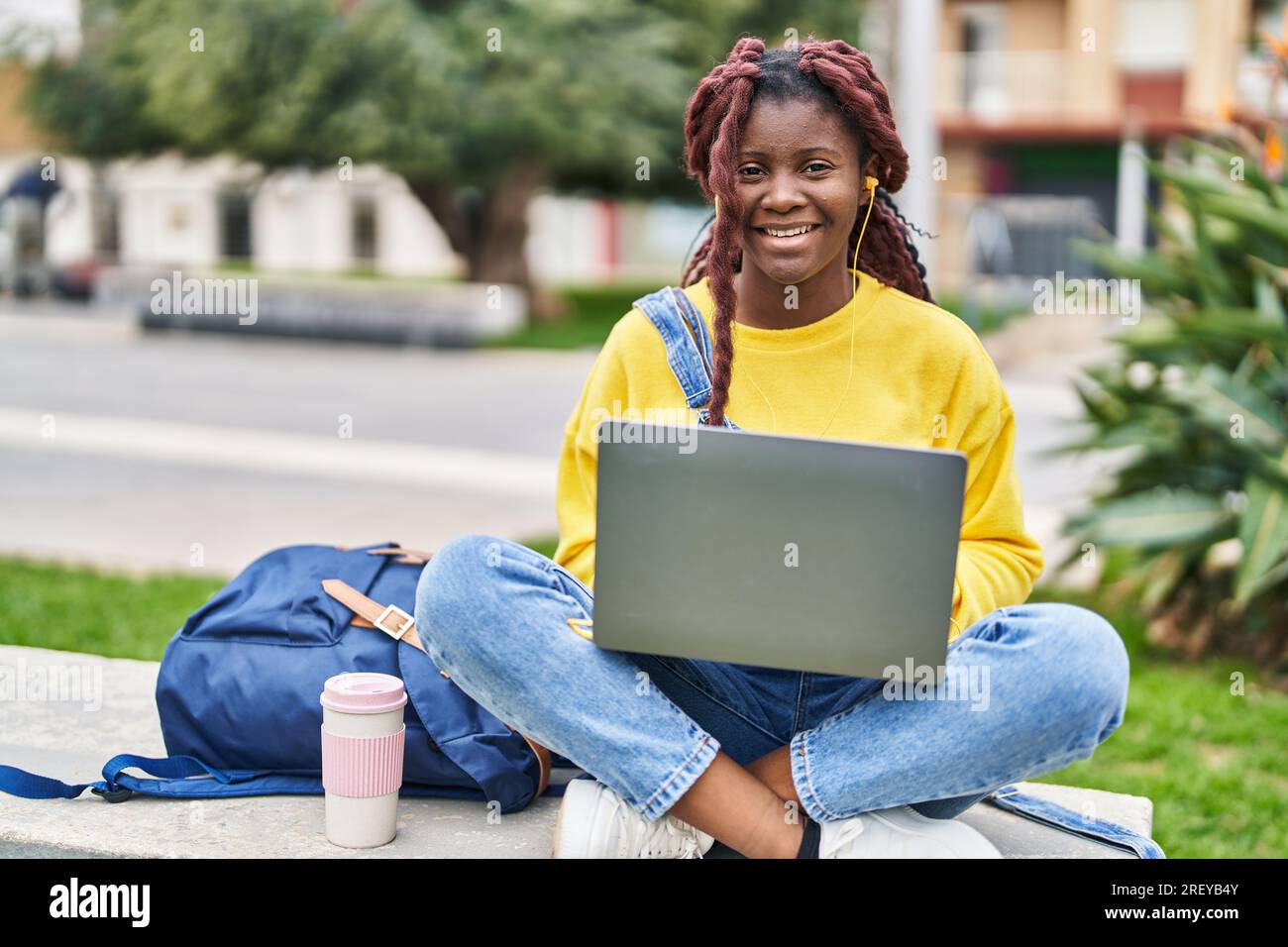 African american woman student using laptop sitting on bench at campus ...