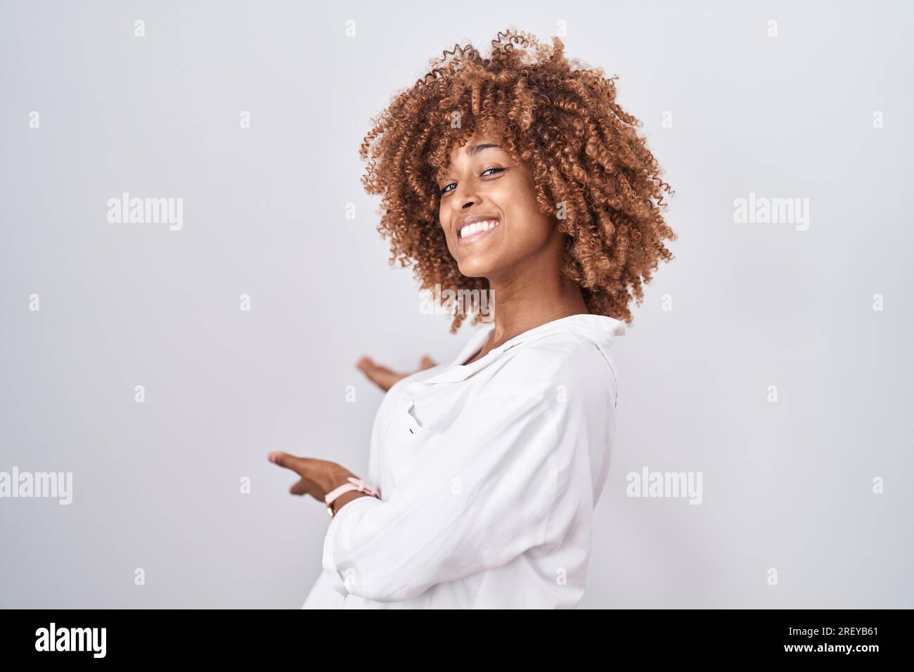 Young hispanic woman with curly hair standing over white background  inviting to enter smiling natural with open hand Stock Photo - Alamy