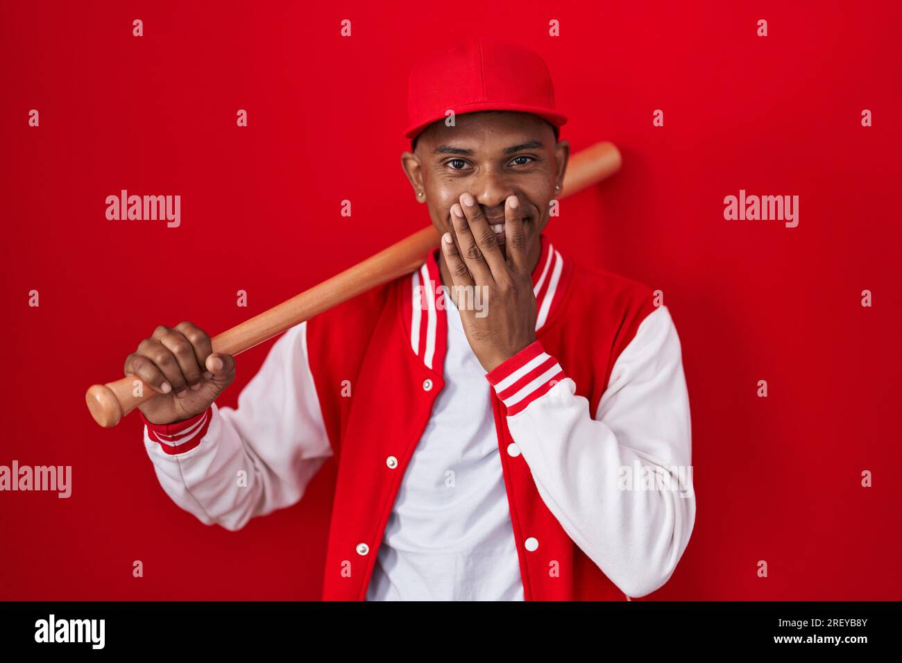 Young hispanic man playing baseball holding bat laughing and