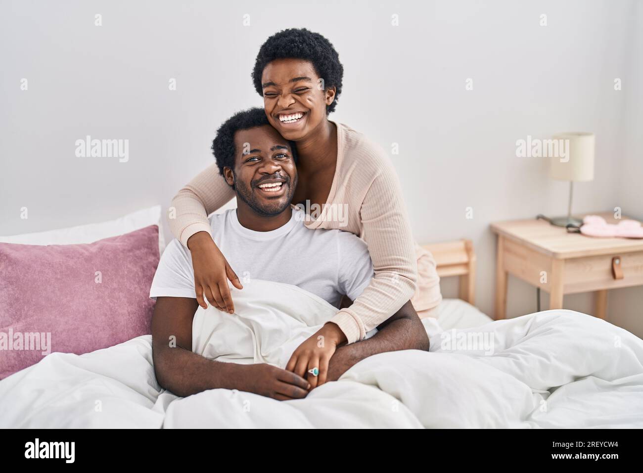 African american man and woman couple hugging each other sitting on bed ...