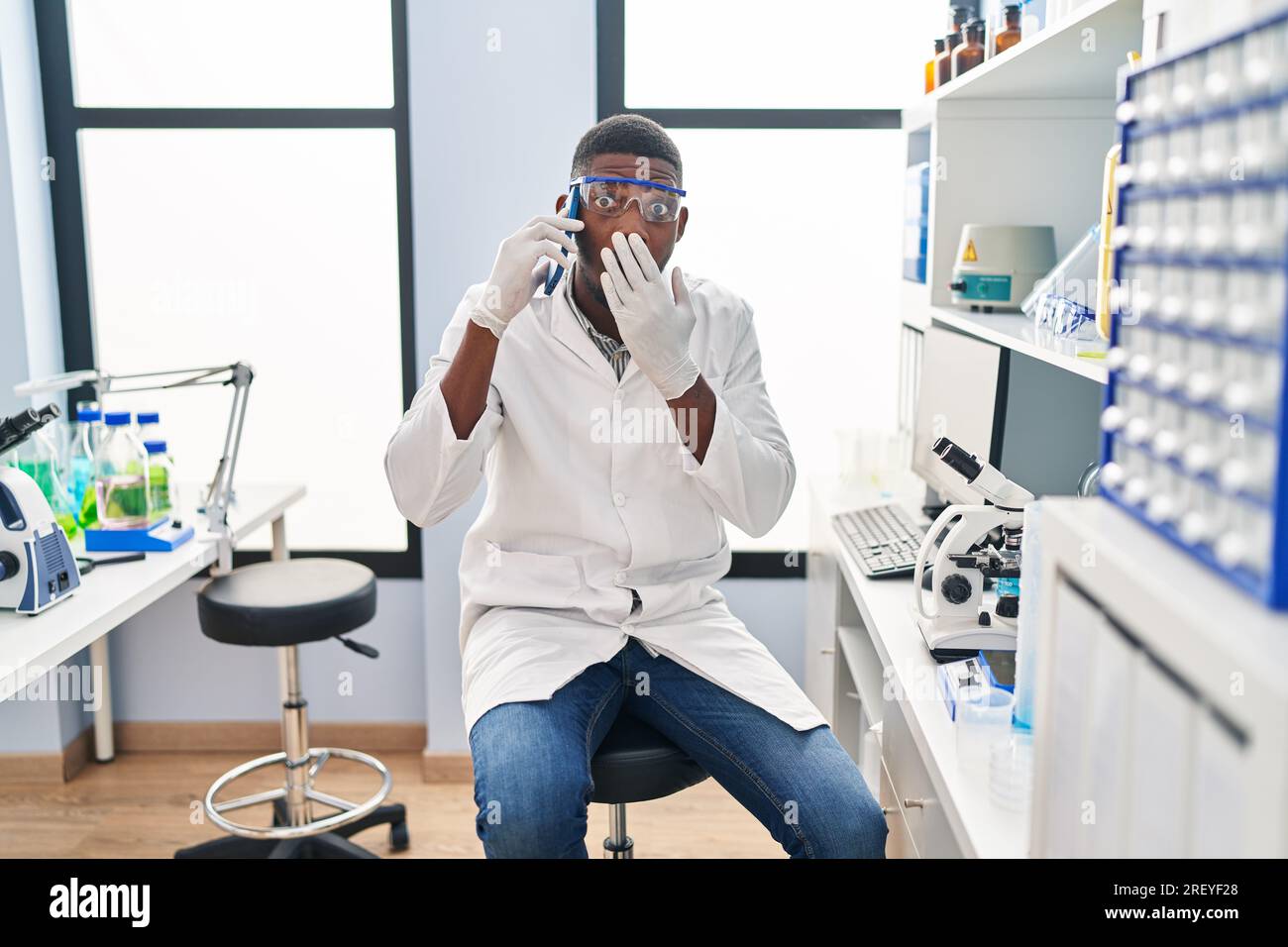 African American Man Working At Scientist Laboratory Speaking On The Phone Covering Mouth With 