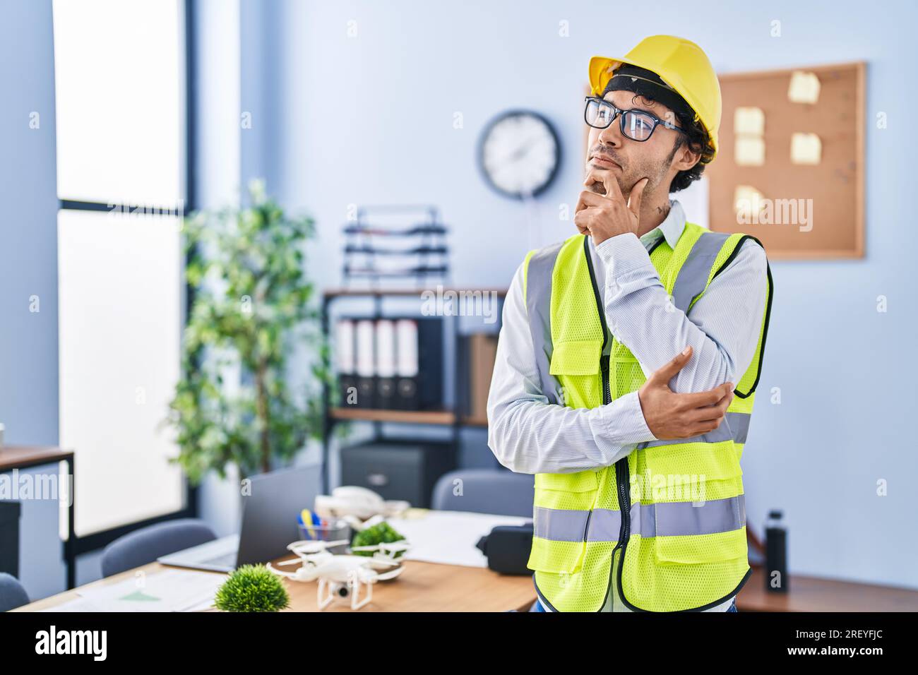 Hispanic man wearing architect hardhat thinking concentrated about doubt with finger on chin and looking up wondering Stock Photo