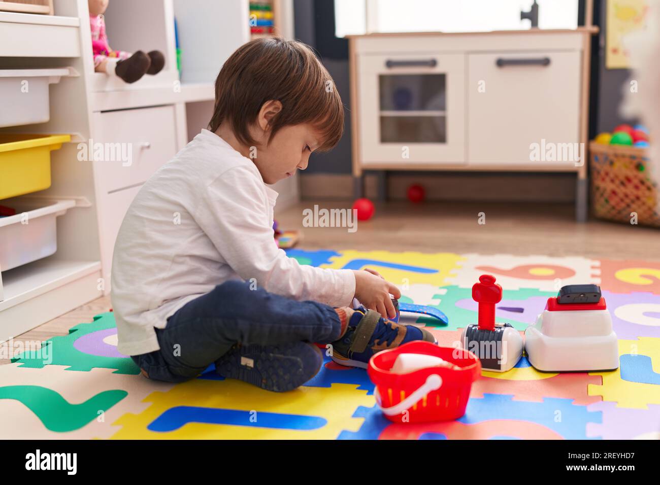 Adorable caucasian boy playing with supermarket toy sitting on floor at ...