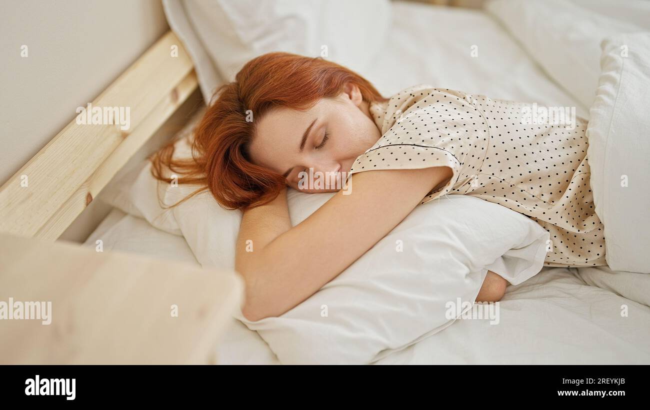 Young redhead woman lying on bed hugging pillow sleeping at bedroom