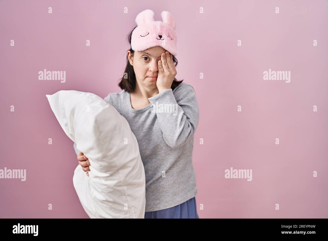 Woman with down syndrome wearing sleeping mask hugging pillow yawning