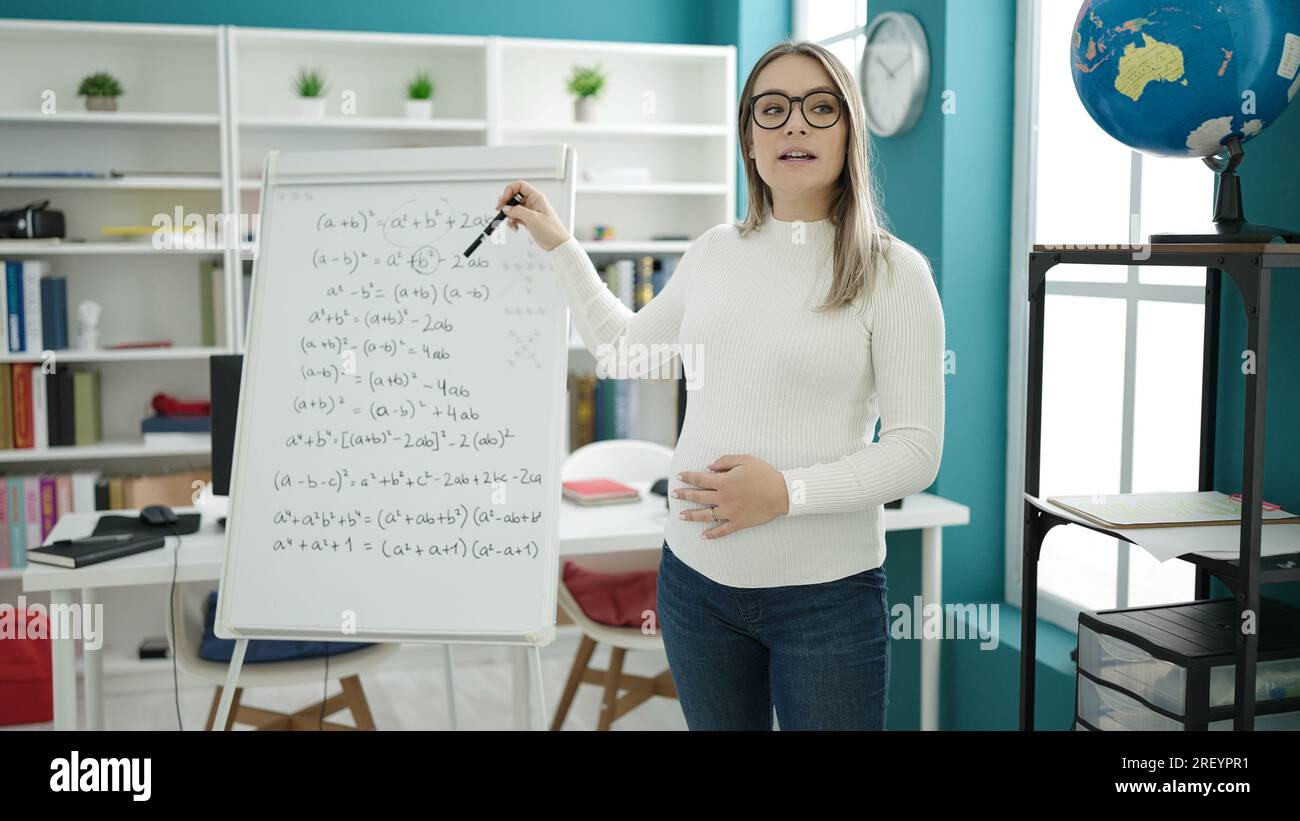 Young pregnant woman teaching maths on magnetic board touching belly at