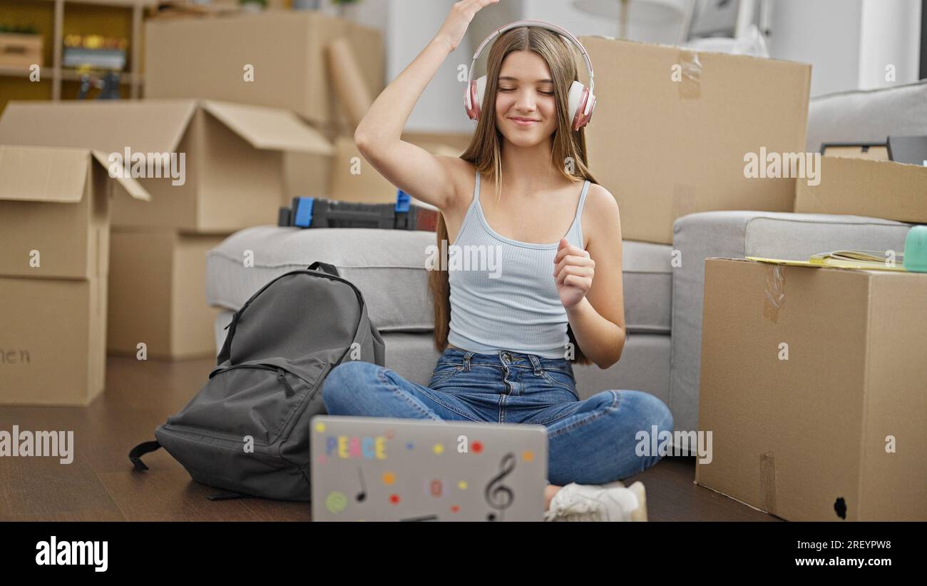 Young beautiful girl student listening to music sitting on floor ...