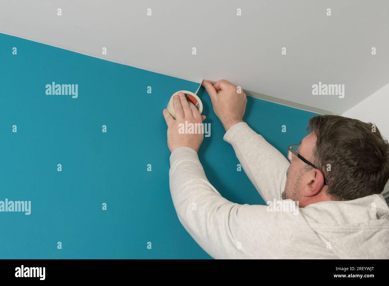 Applying masking tape to a white ceiling before painting the wall a different color Stock Photo