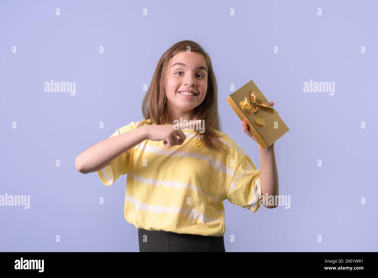 Joyful teenage girl holds a gift in a gilded package with a bow in her hands. lilac background Stock Photo