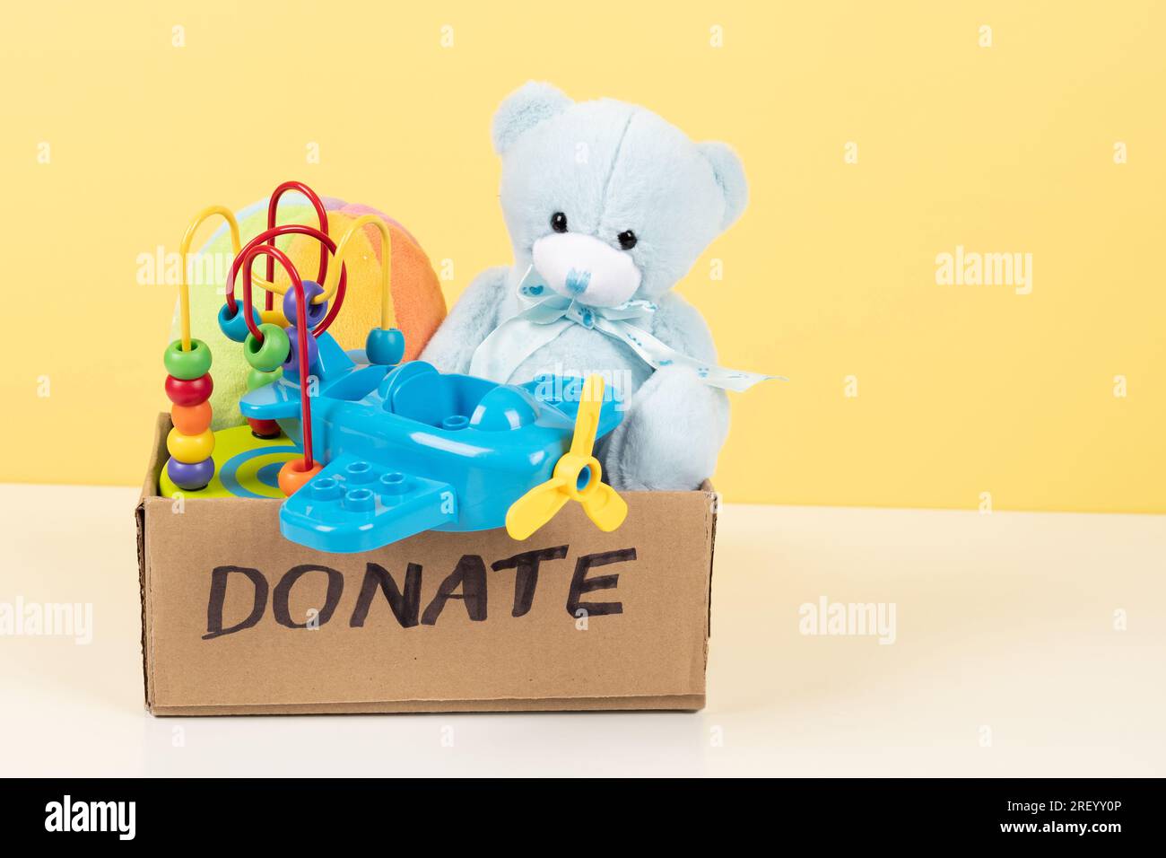 Donation, charity concept. Toy donation box with teddy bear, wooden and plastic educational toys on white desk Stock Photo