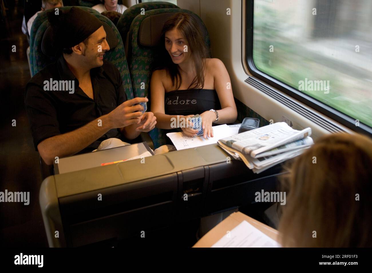 Two people conversing and playing cards on a train, with newspapers and documents on the table. Stock Photo
