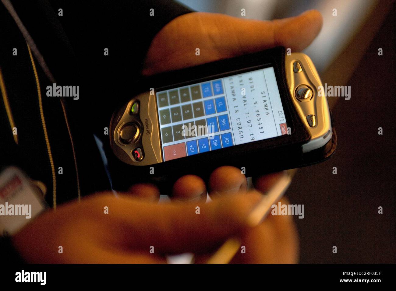 An individual operates a Pocket PC device using a stylus, displaying a grid-like interface with numeric options. Stock Photo