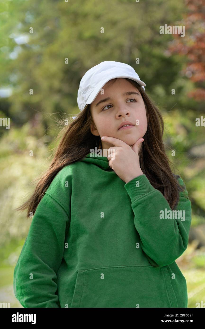 Walk in the forest park. Portrait of a teenage girl on the background of an autumn park. In a thoughtful pose. White baseball cap, green sweater Stock Photo