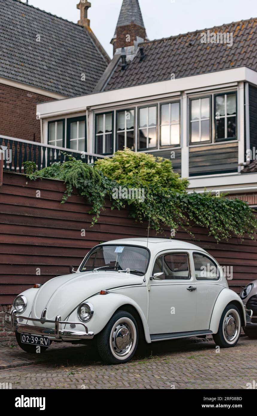 Enkhuizen, the Netherlands - July 29th 2023: A pristine white 1971 Volkswagen Beetle parked besides a beautiful 1930's house. Stock Photo
