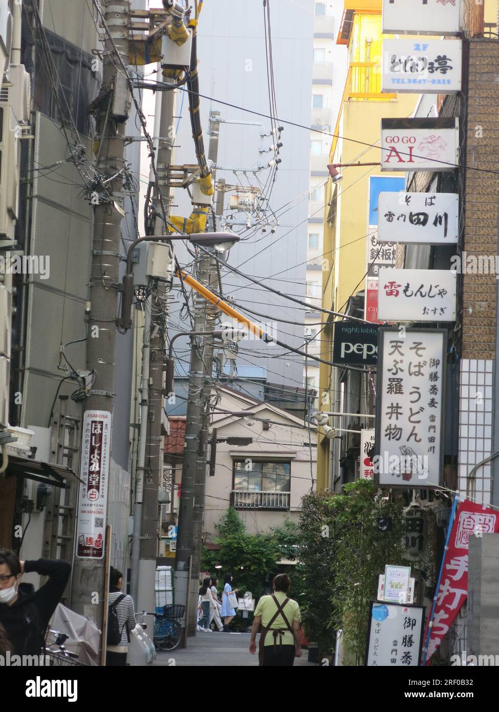 A city street in Asakusa, Tokyo, showing the plethora of power supply pylons & electricity wires and lots of signs in Japanese script. Stock Photo