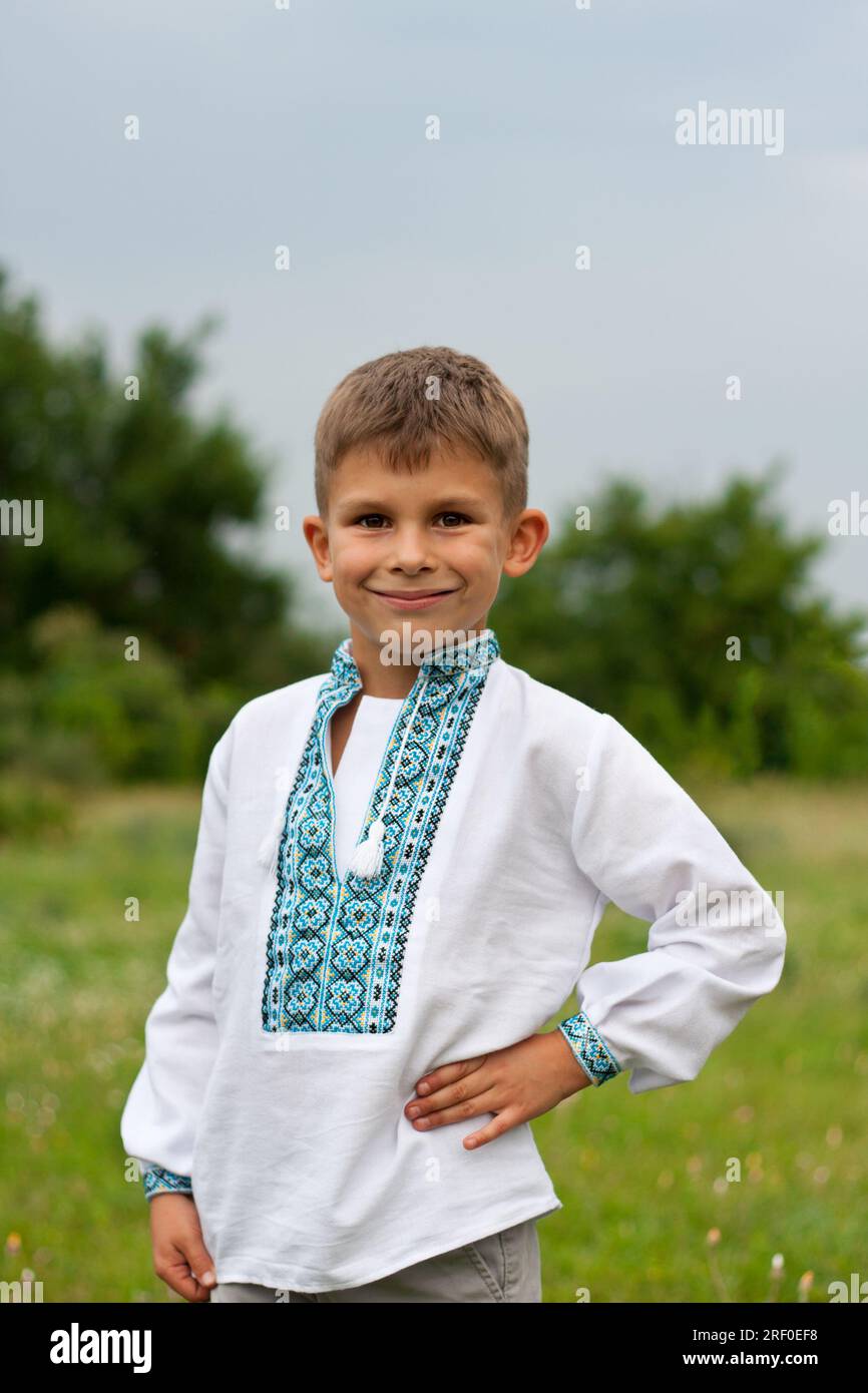 Portrait of happy Ukrainian preschool boy in traditional national vyshyvanka, standing in meadow. Summertime. Pride to be Ukrainian. Embroidery day. I Stock Photo