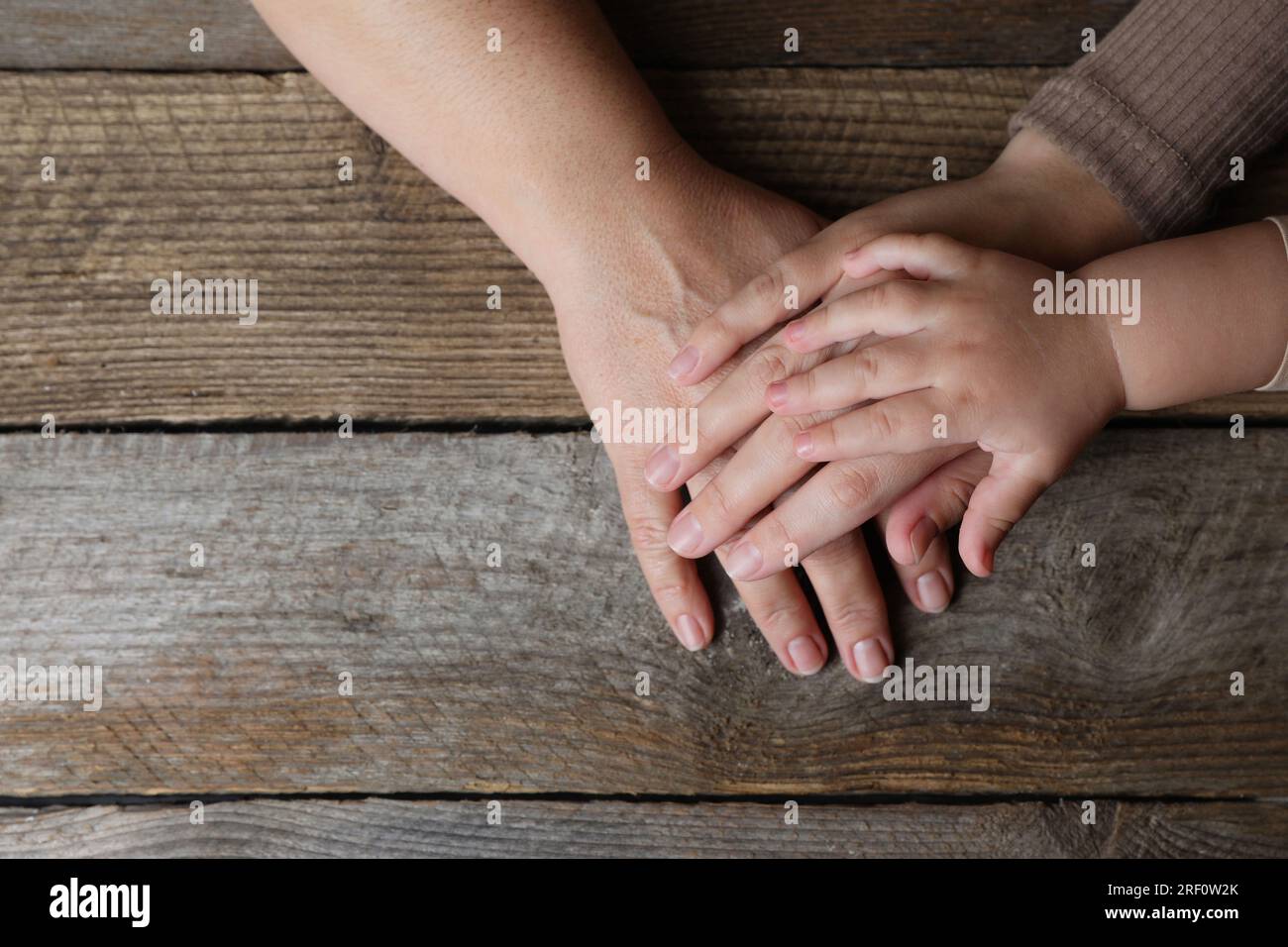 Family holding hands together at wooden table, top view. Space for text ...