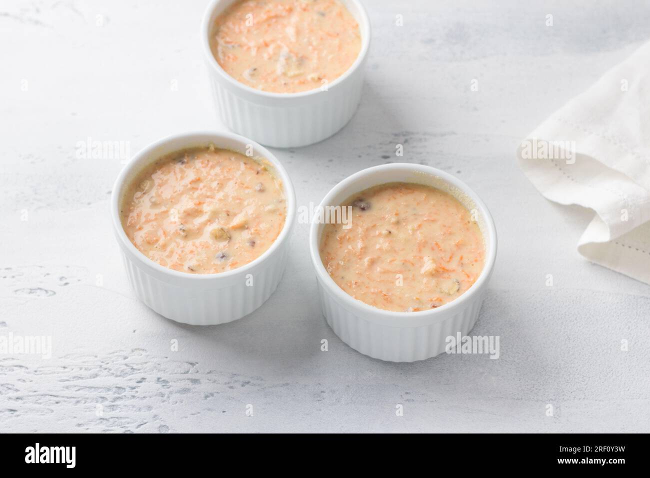 Dough for carrot semolina cake or mannik with nuts in baking dishes. cooking on a light blue background. step by step, cooking step Stock Photo