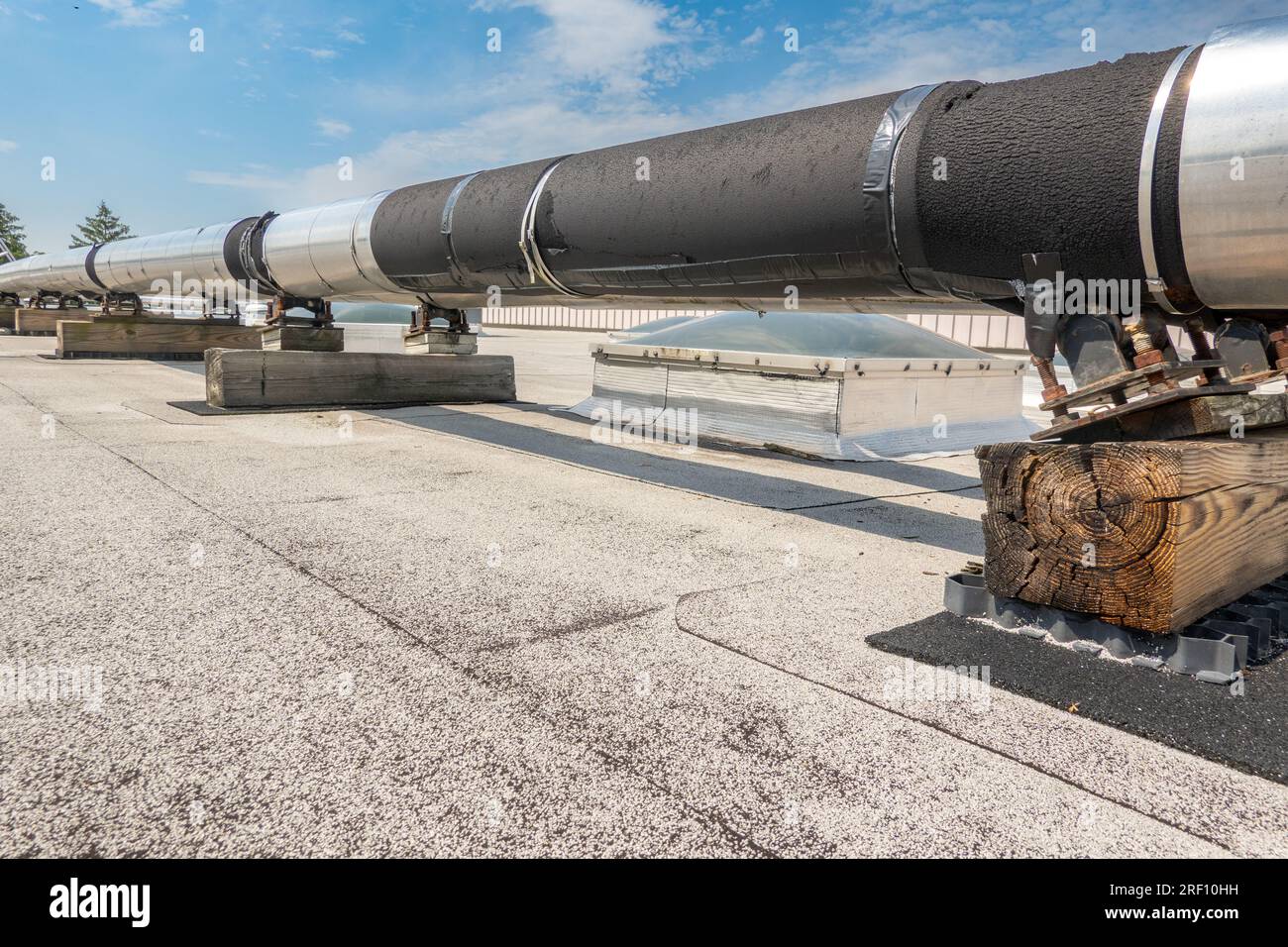 Roof mounted industrial insulated HVAC pipes on gray roof and wooden