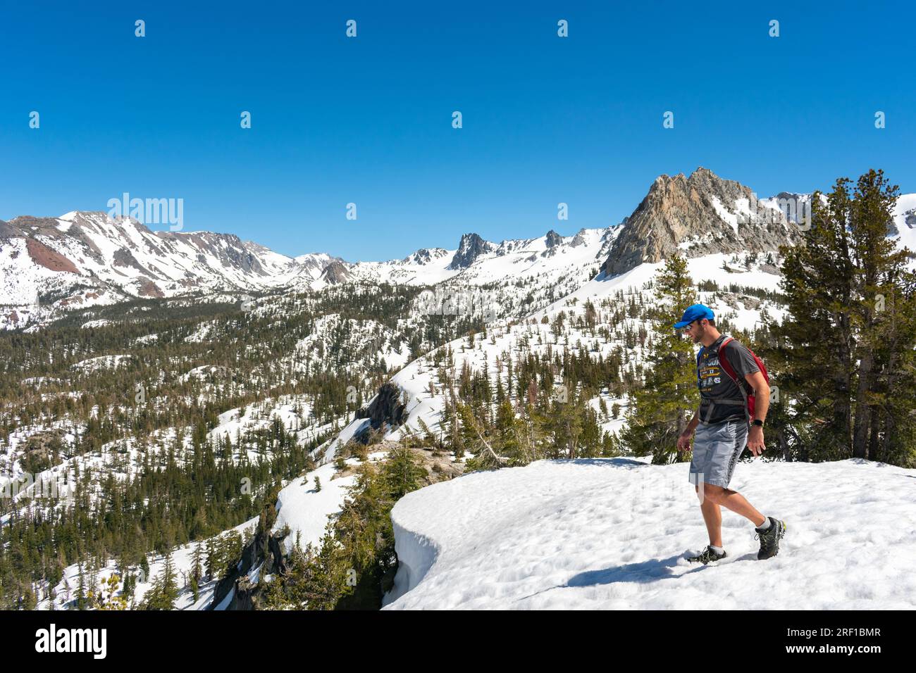 An adventurer enjoys a serene hike through the melting snow paths of Mammoth Lakes, surrounded by majestic, snow-dusted peaks under a brilliant blue s Stock Photo