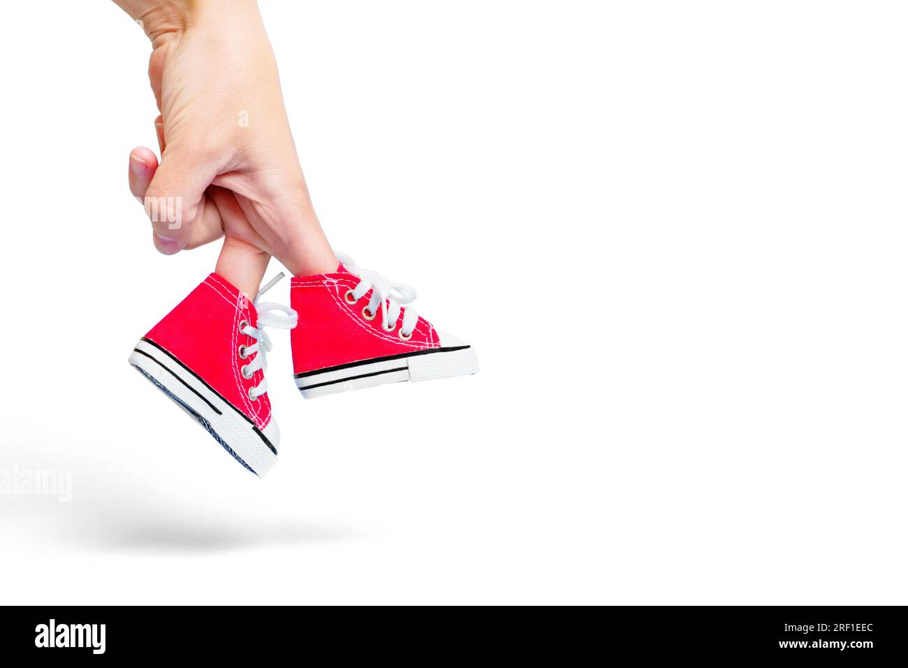 Closeup of a female hand with the fingers wearing a pair of red canvas shoes with white laces