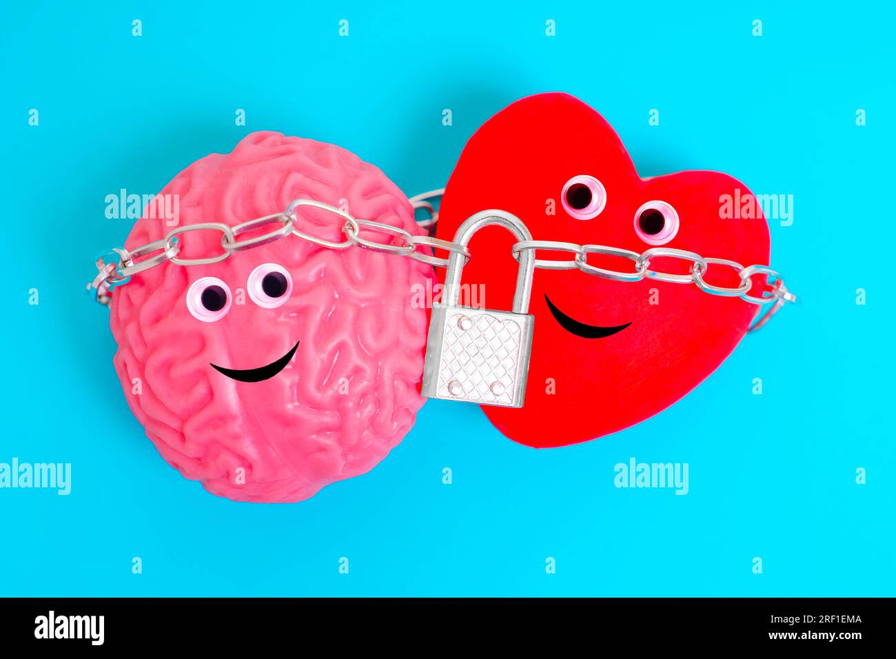 Cute anthropomorphic heart and brain characters, bound tightly together by a chain and secured with a padlock isolated on blue background. Intellect a Stock Photo