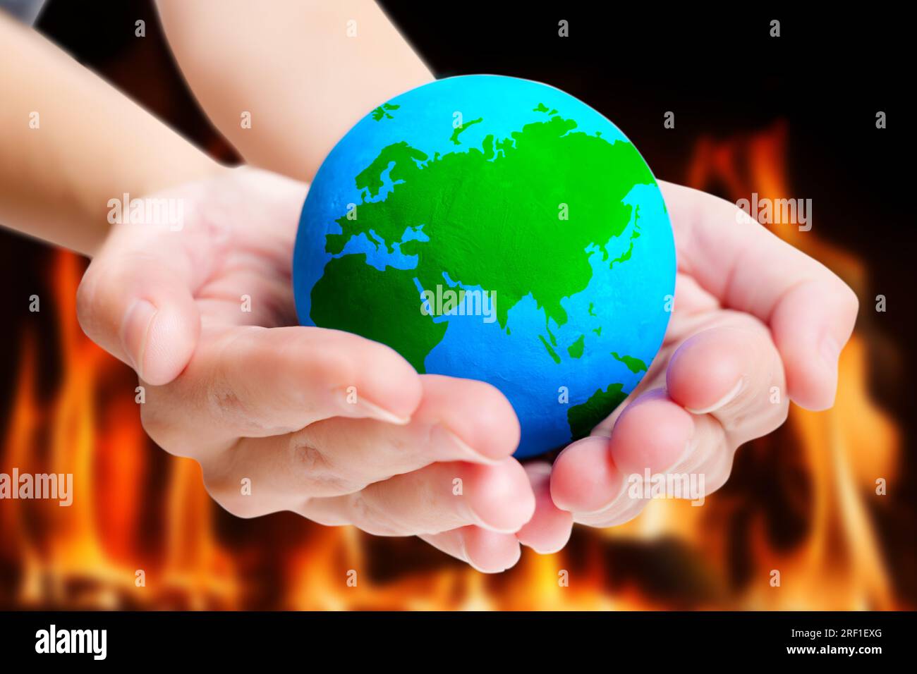 Blue and green model of the Earth held in hands against a backdrop of flames. Concept of environmental activism and the need for immediate action. Stock Photo