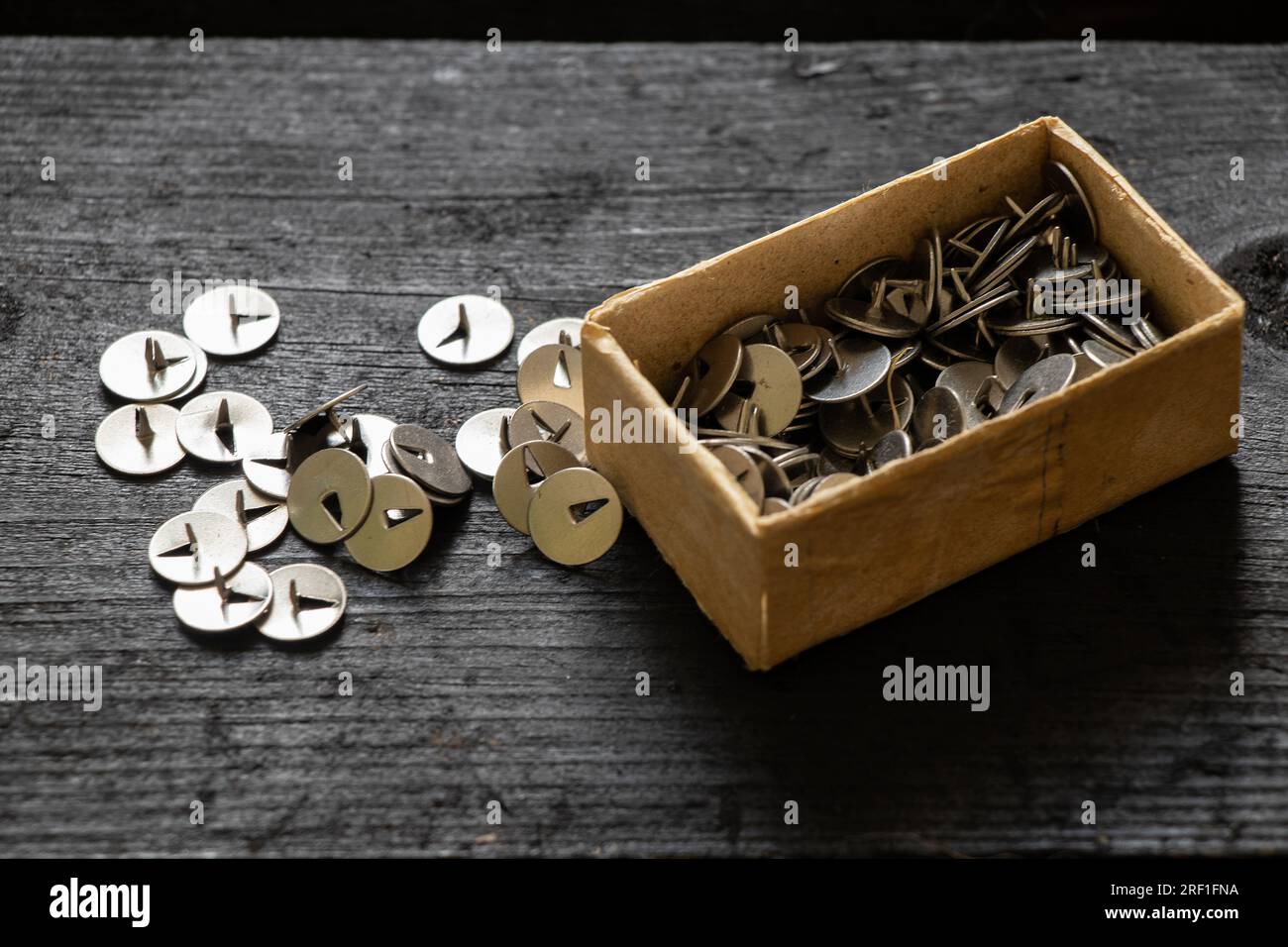 Old round metal paper clips lie on a black wooden table next to it a paper box with paper clips, stationery Stock Photo