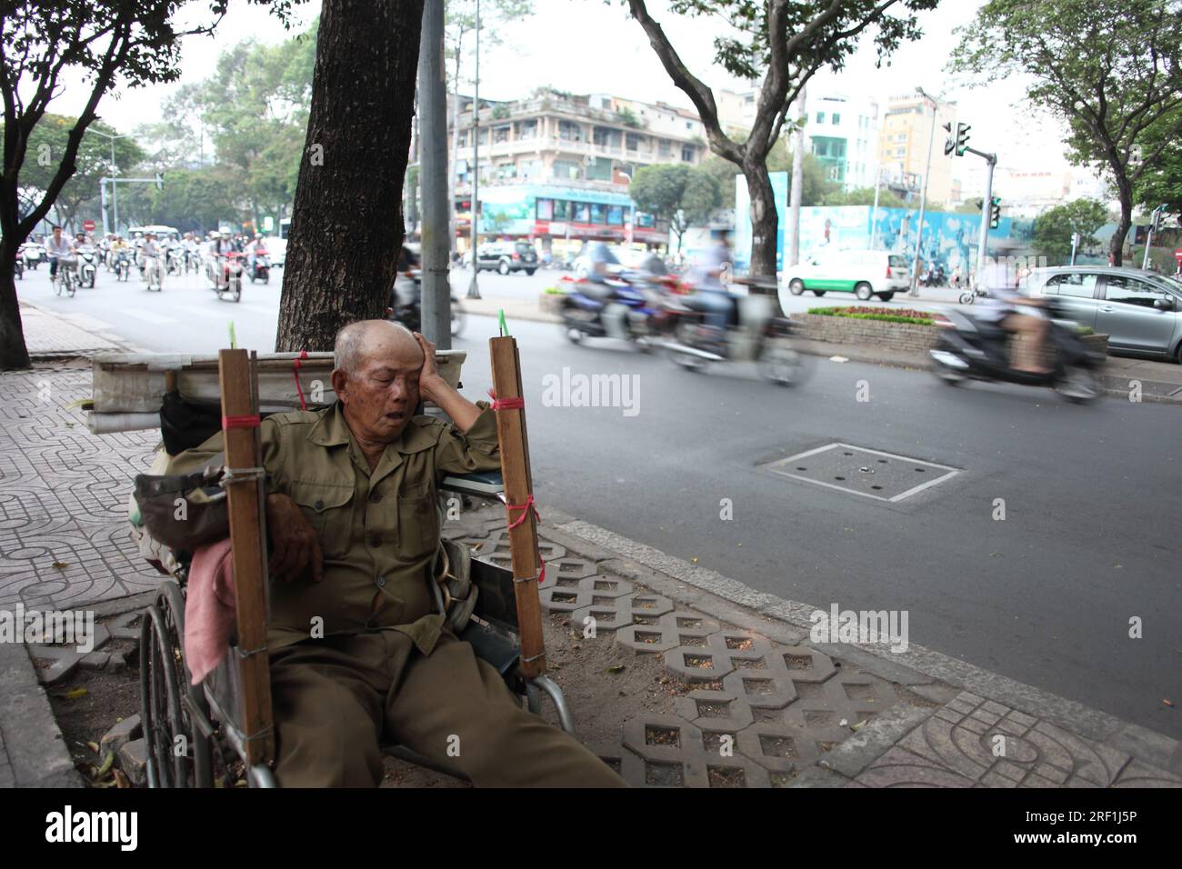 Elderly Vietnamese man sleeping in a wheelchair on the noisy road side