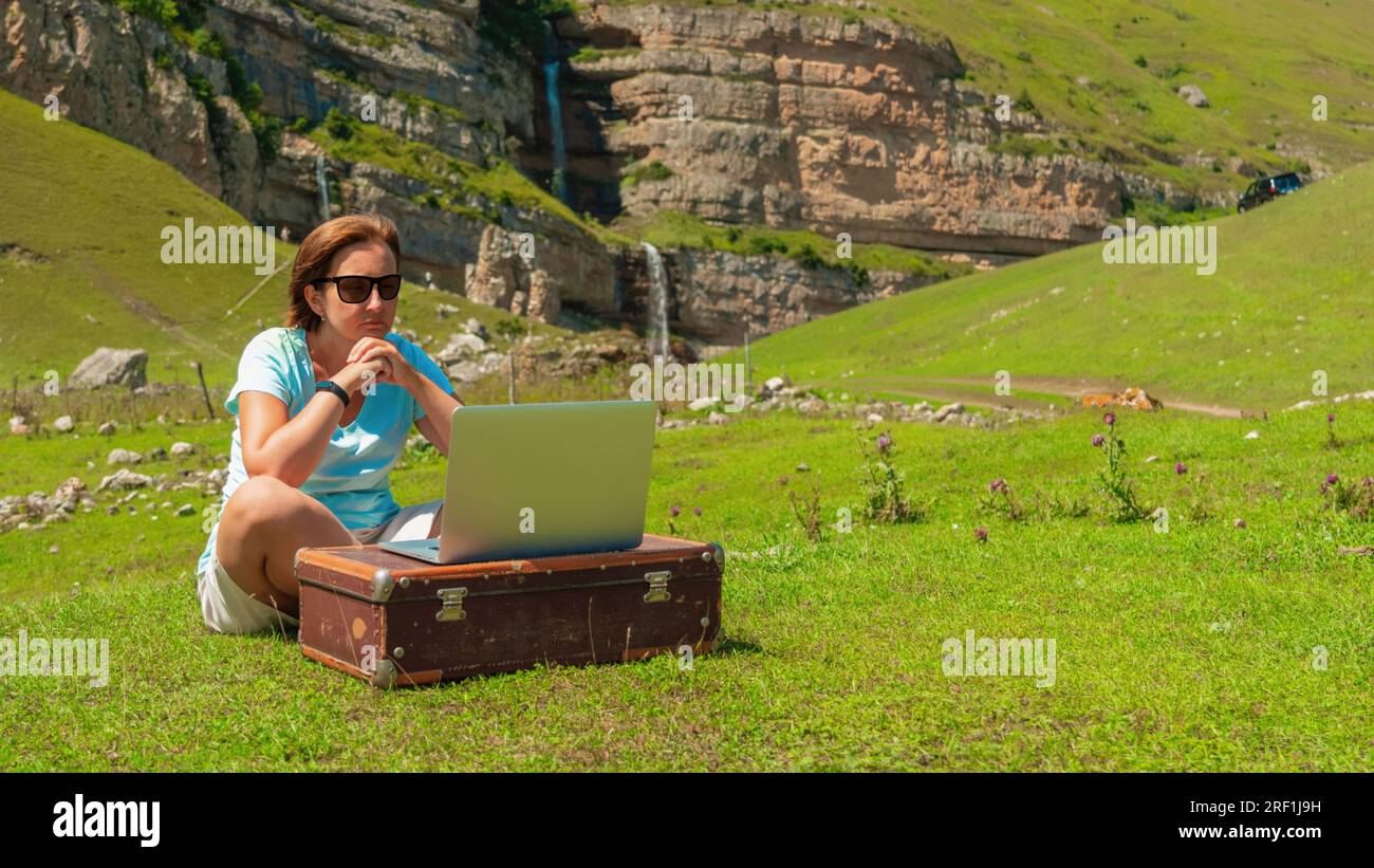 Young woman at work on a laptop in nature in the mountains Stock Photo