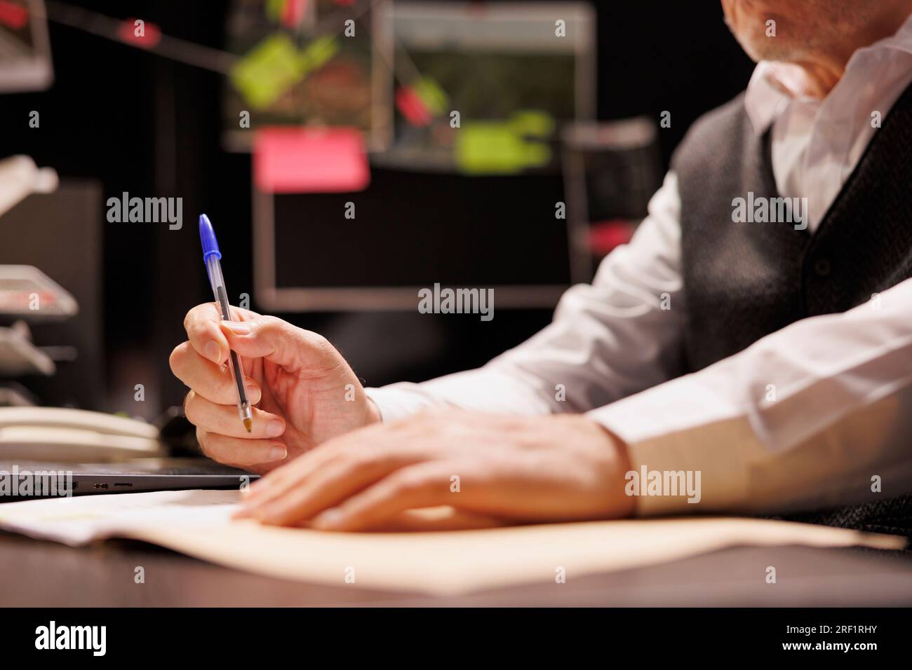 Senior police officer writing missing person case report, working overhours at criminal case in arhive room. Old investigator analyzing criminology files, planning startegy to catch suspect. Close up Stock Photo
