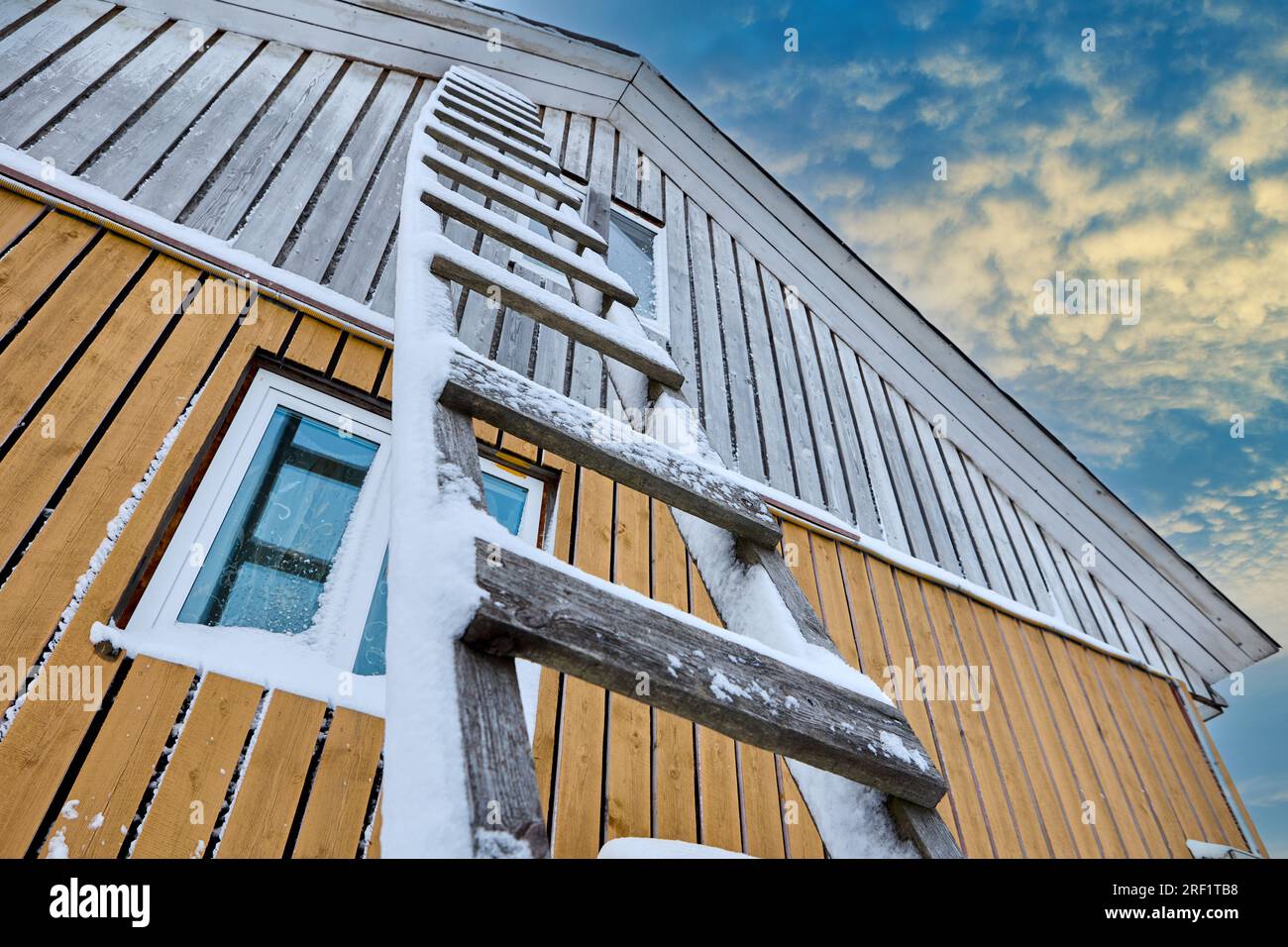 Wooden scaling ladder with steps is leaning against wall of wooden country house in winter. Stock Photo