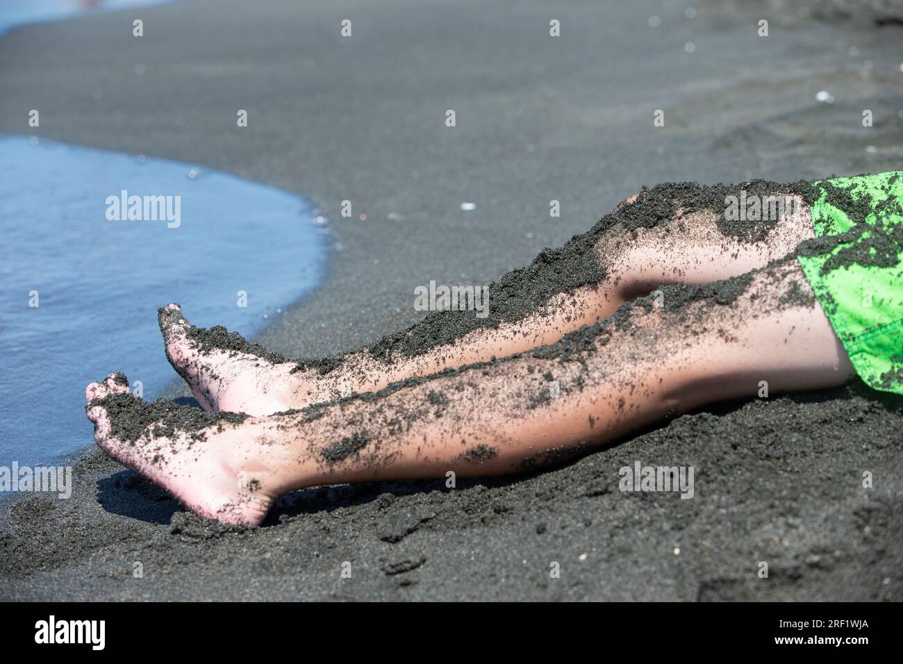 The child's feet are covered with therapeutic black magnetic sand. Stock Photo