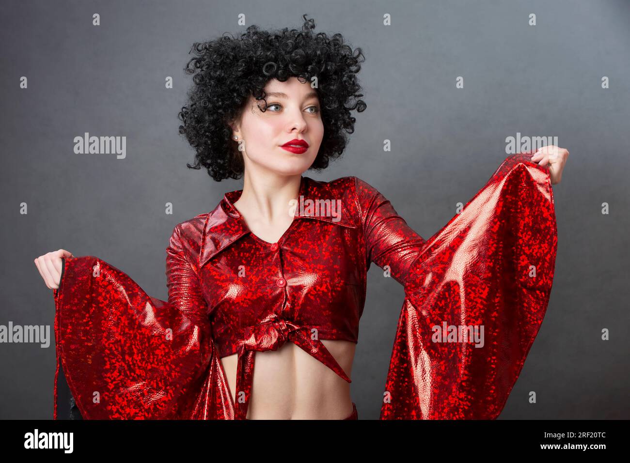 Vintage woman in afro wig and red disco costume on a gray background. Girl in the style of the seventies. Stock Photo
