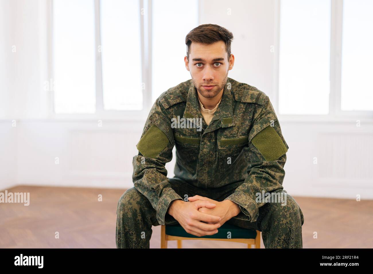 Portrait of stressed soldier male in camouflage uniform sitting in circle during PTSD group therapy session looking at camera with serious expression. Stock Photo