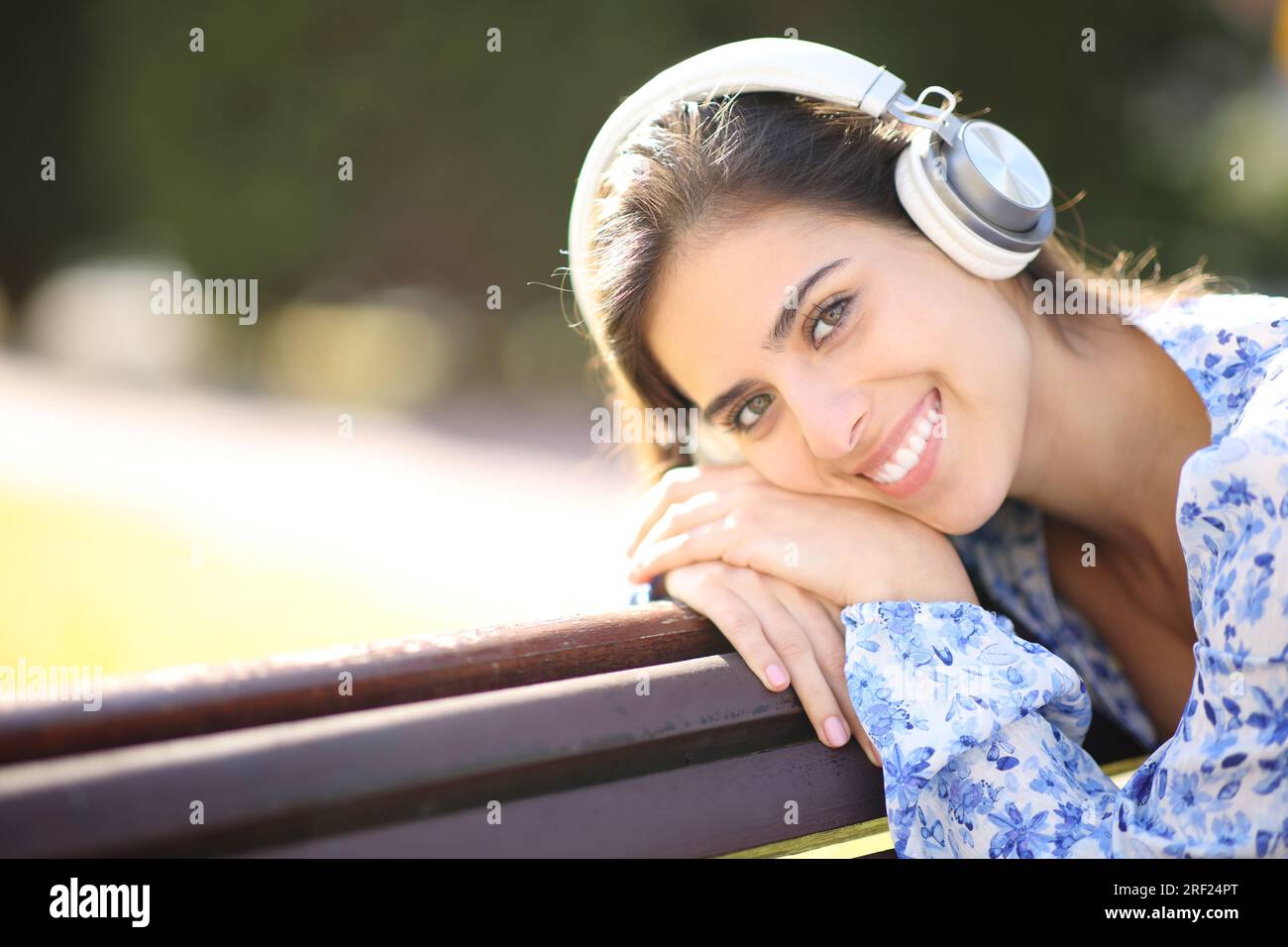 Beautiful portrait of a woman wearing headphone on a bench in a park looking at you Stock Photo