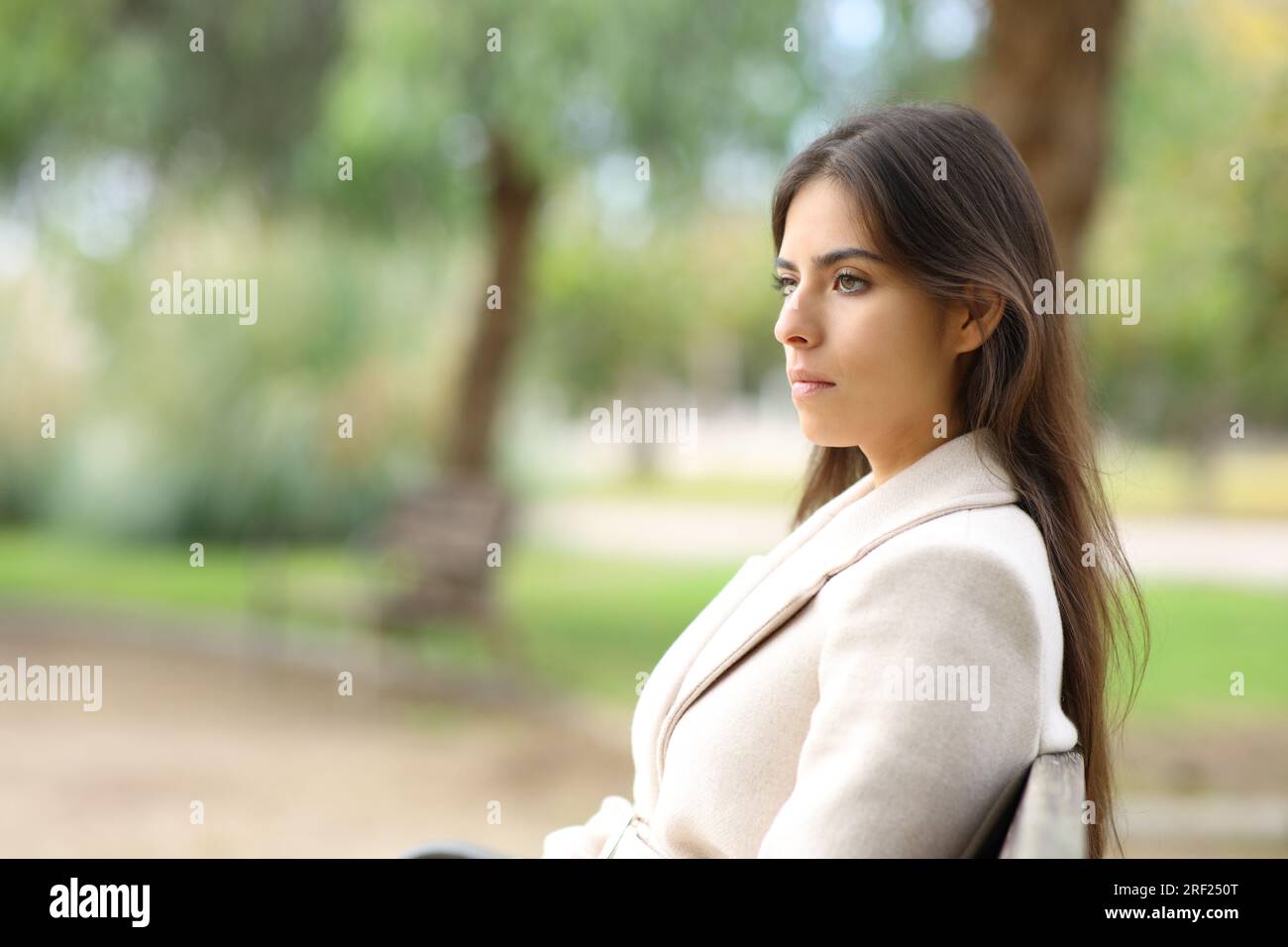 Serious woman in winter looks away on a bench in a park Stock Photo