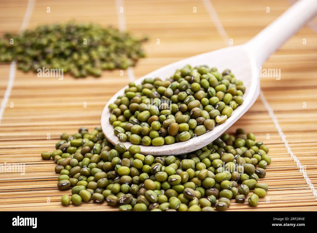 A wooden spoon filled with mung beans on top of a bamboo mat Stock Photo