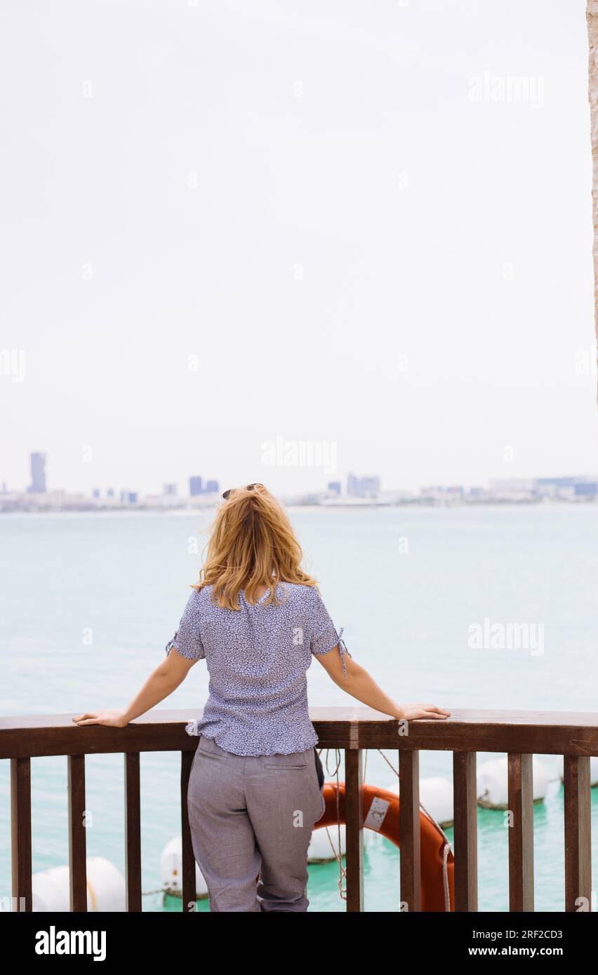 Backview of a blond woman standing and watching the sea Stock Photo
