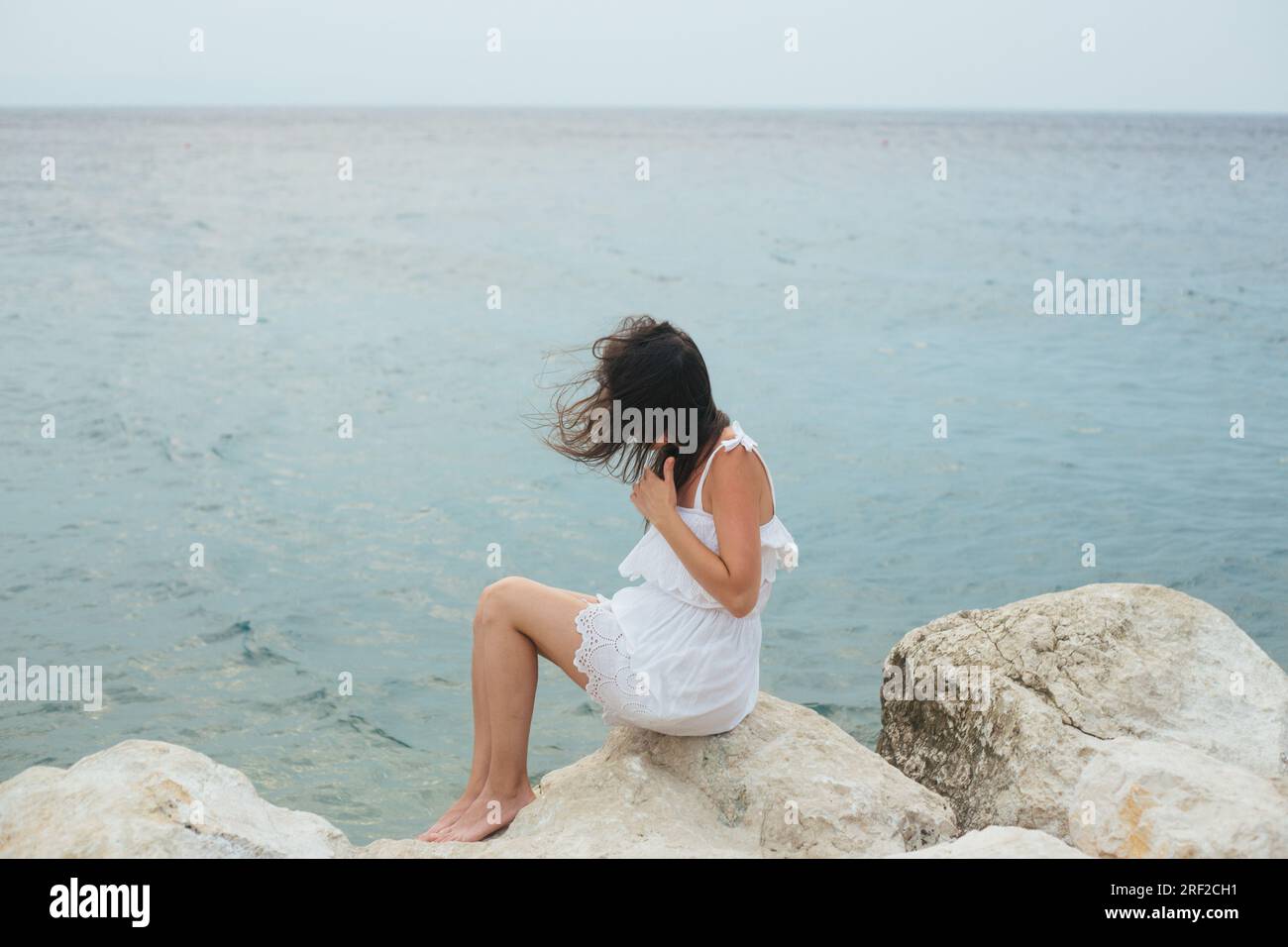 Woman in white dress sitting on the rock above the sea Stock Photo - Alamy