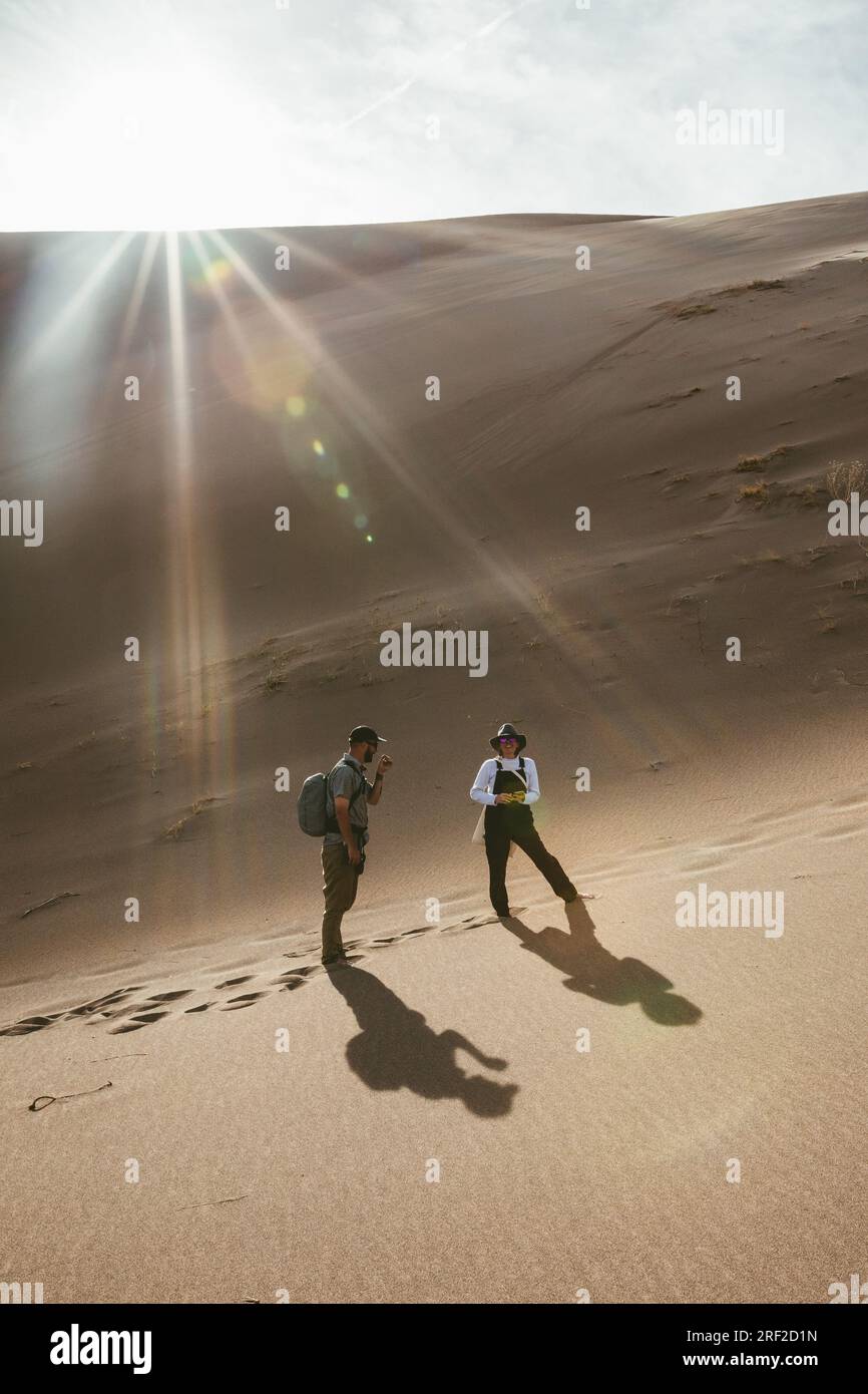 two hikers in sand dunes stop and smile under sun flare Stock Photo