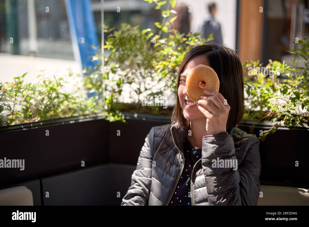 Woman having breakfast and joking with a doughnut on her face Stock Photo