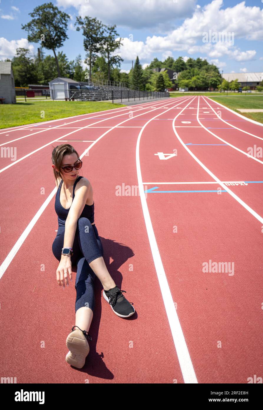 female athlete wearing sunglasses stretches while working out on track