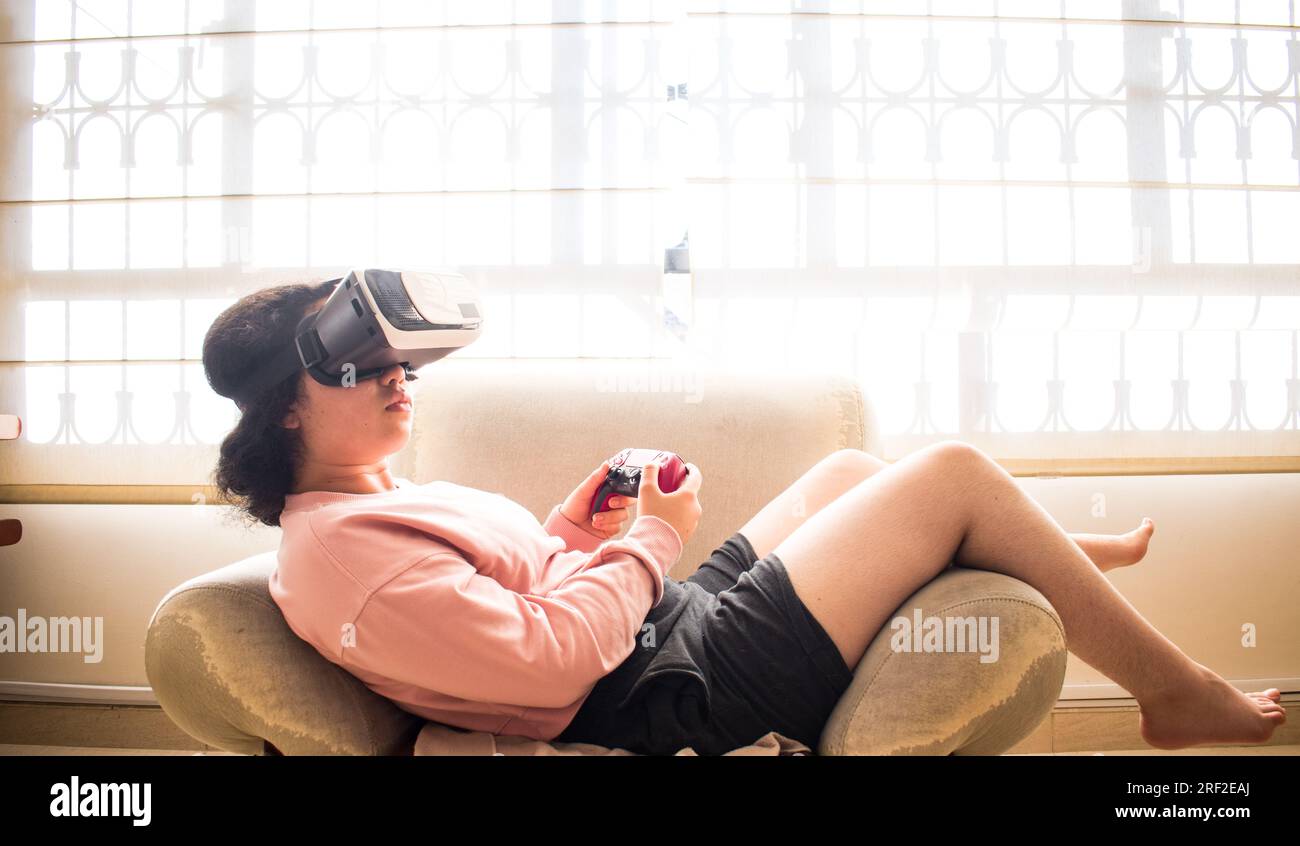Gamer playing on vr headset with video game controller sitting on sofa Stock Photo