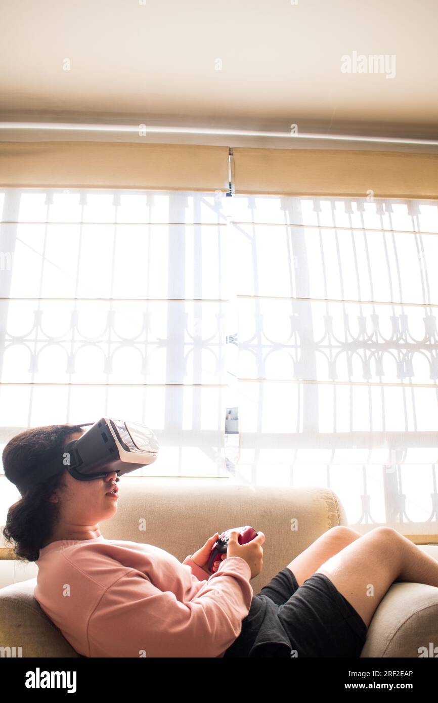 Gamer playing on vr headset with video game controller sitting on sofa Stock Photo